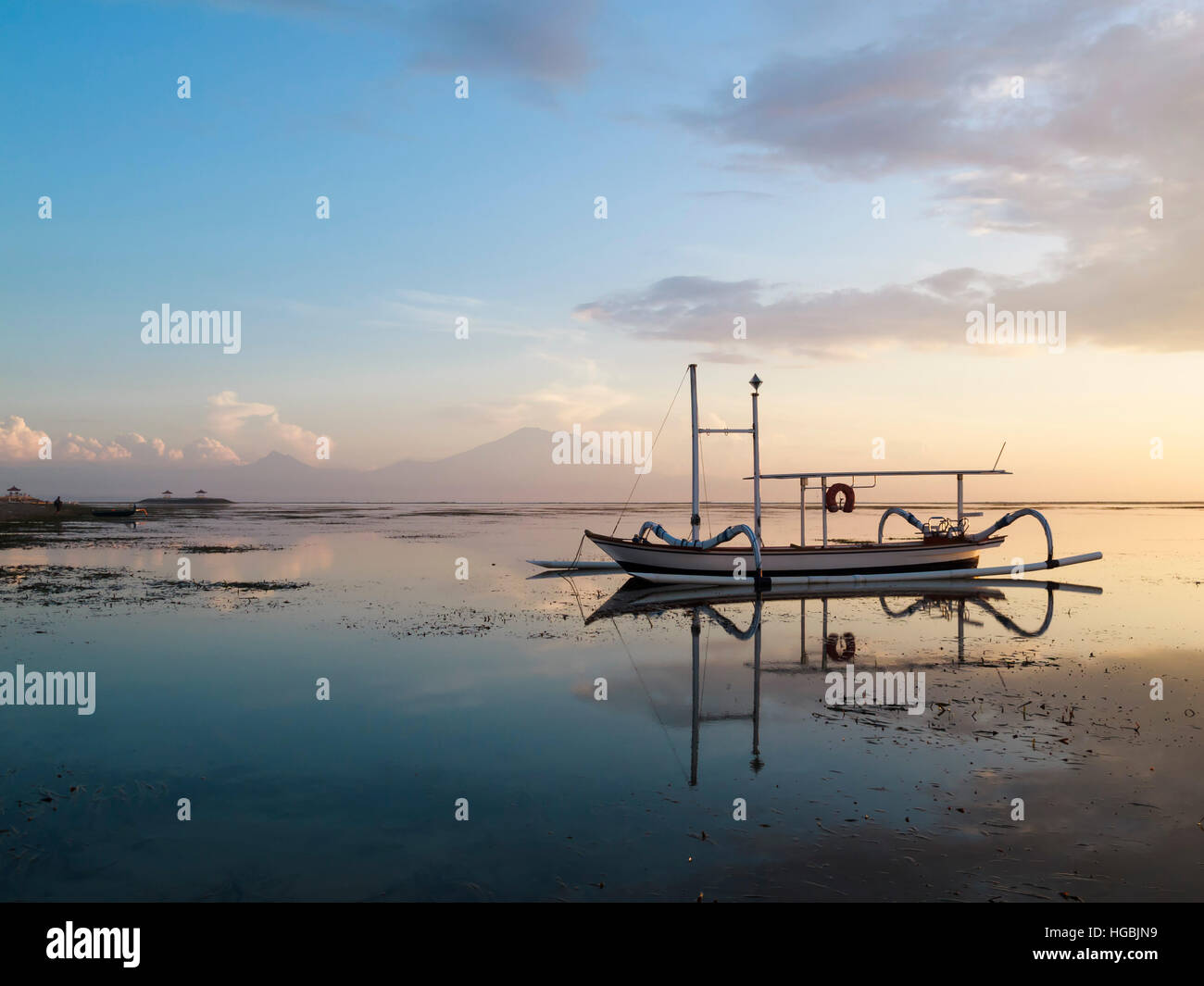 Bali traditional fishing boat reflected in the calm waters at sunset. Stock Photo