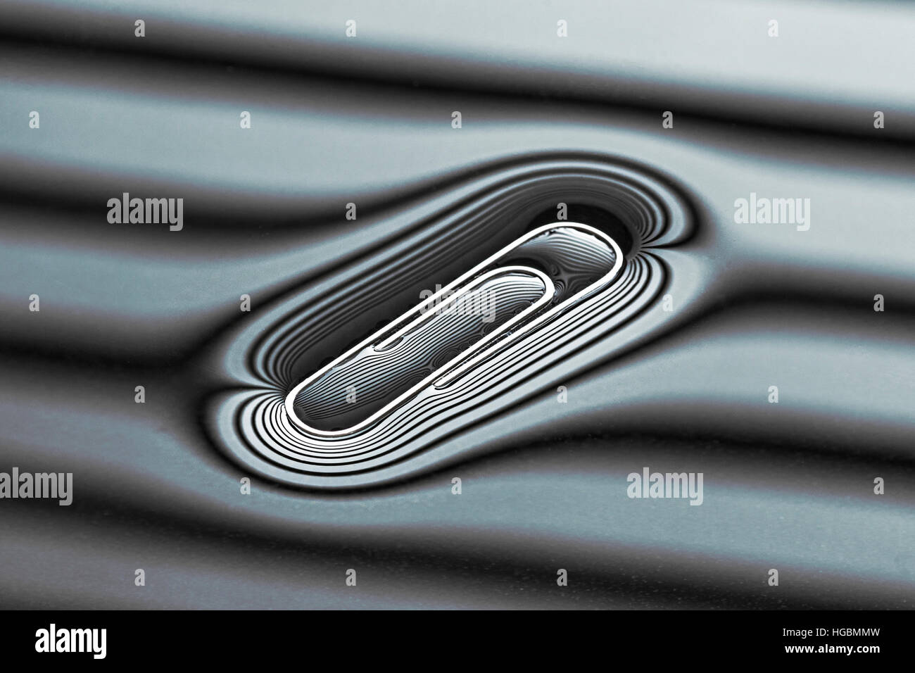 Floating Paperclip.  Paper clip floating on water courtesy of surface tension. Shape of surface water caught in the reflected lines on the surface. Stock Photo