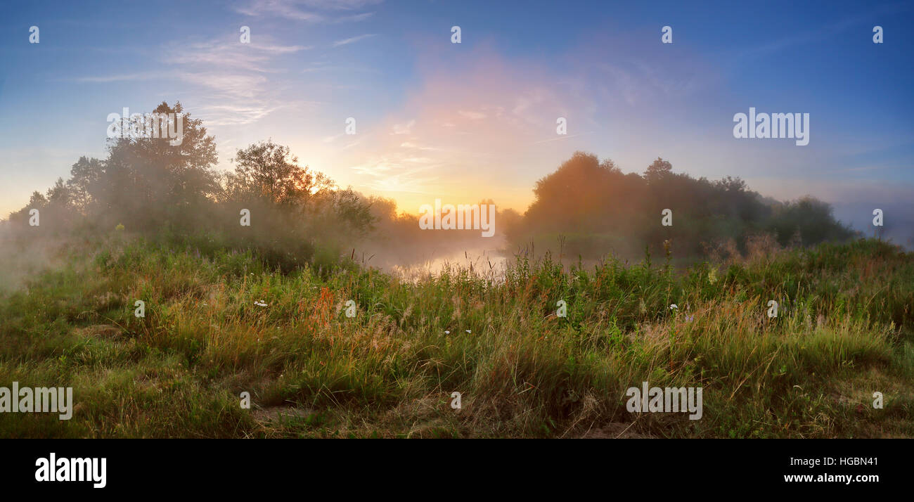 Summer misty sunrise on the river. Foggy river in the morning. Misty morning panorama. Stock Photo
