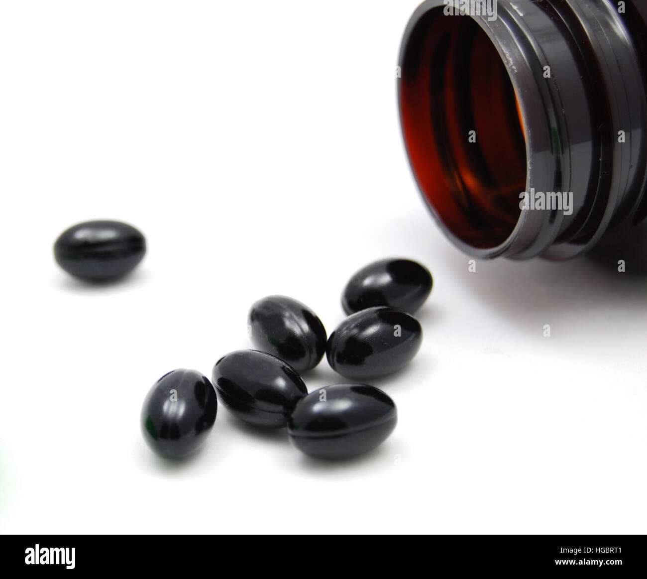 Sleeping pills or liquid herbs in a soft gel capsule spilling from a bottle. Stock Photo
