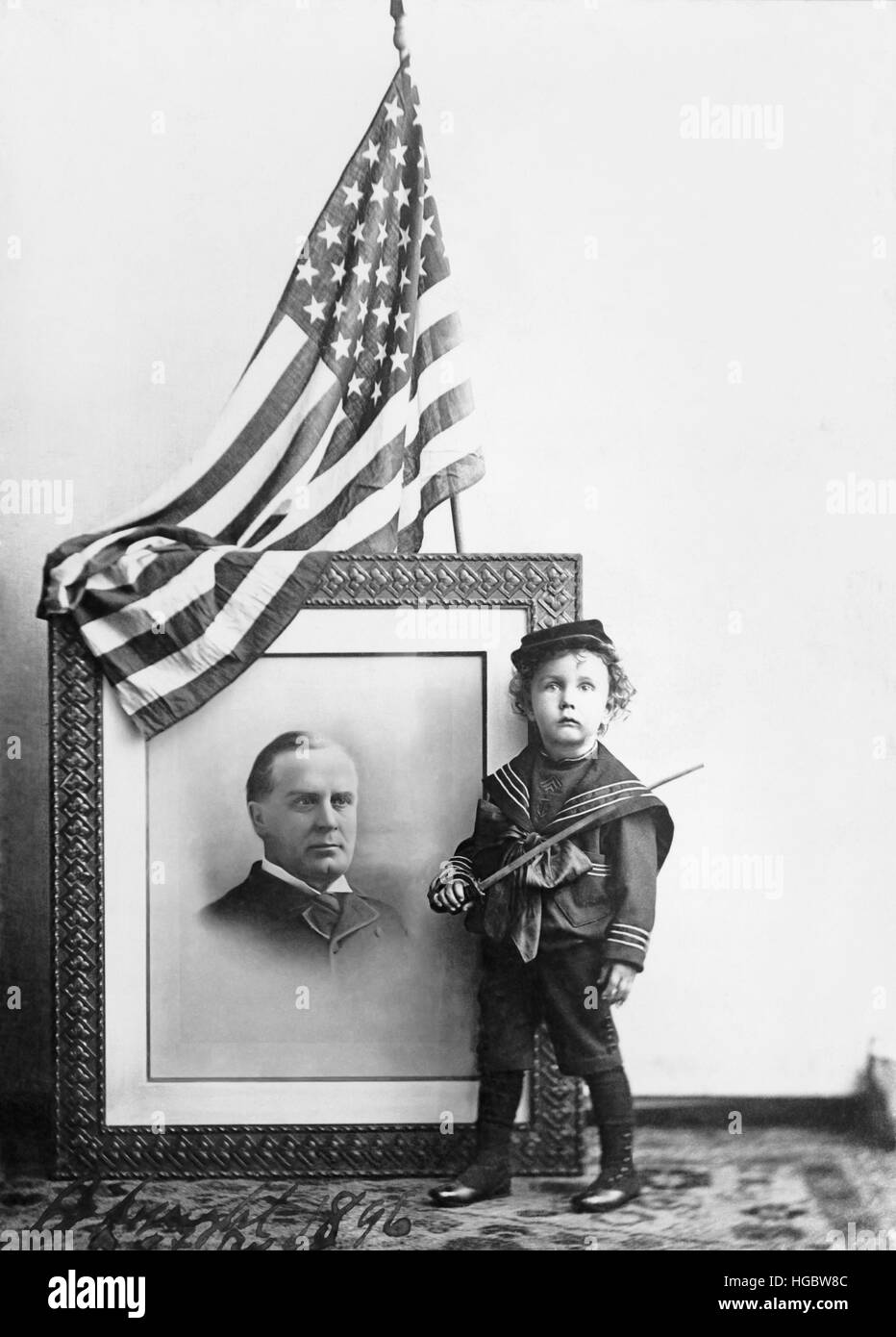 Boy in sailor uniform standing by a portrait of William McKinley. Stock Photo