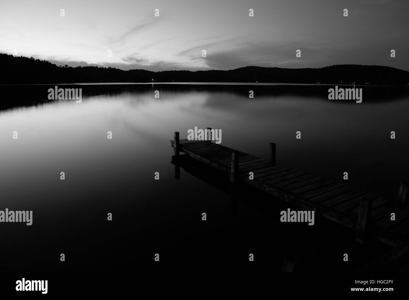 Old wooden jetty at night on a mirror calm lake with reflections and silhouettes long exposure monochrome Stock Photo
