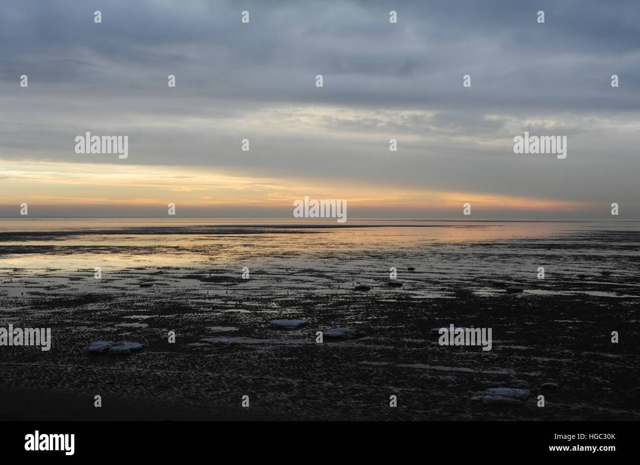 Sand beach with isolated sea ice blocks towards Southport Coastline and red sunset opening in grey clouds, St Annes, Fylde Coast, Lancashire, UK Stock Photo