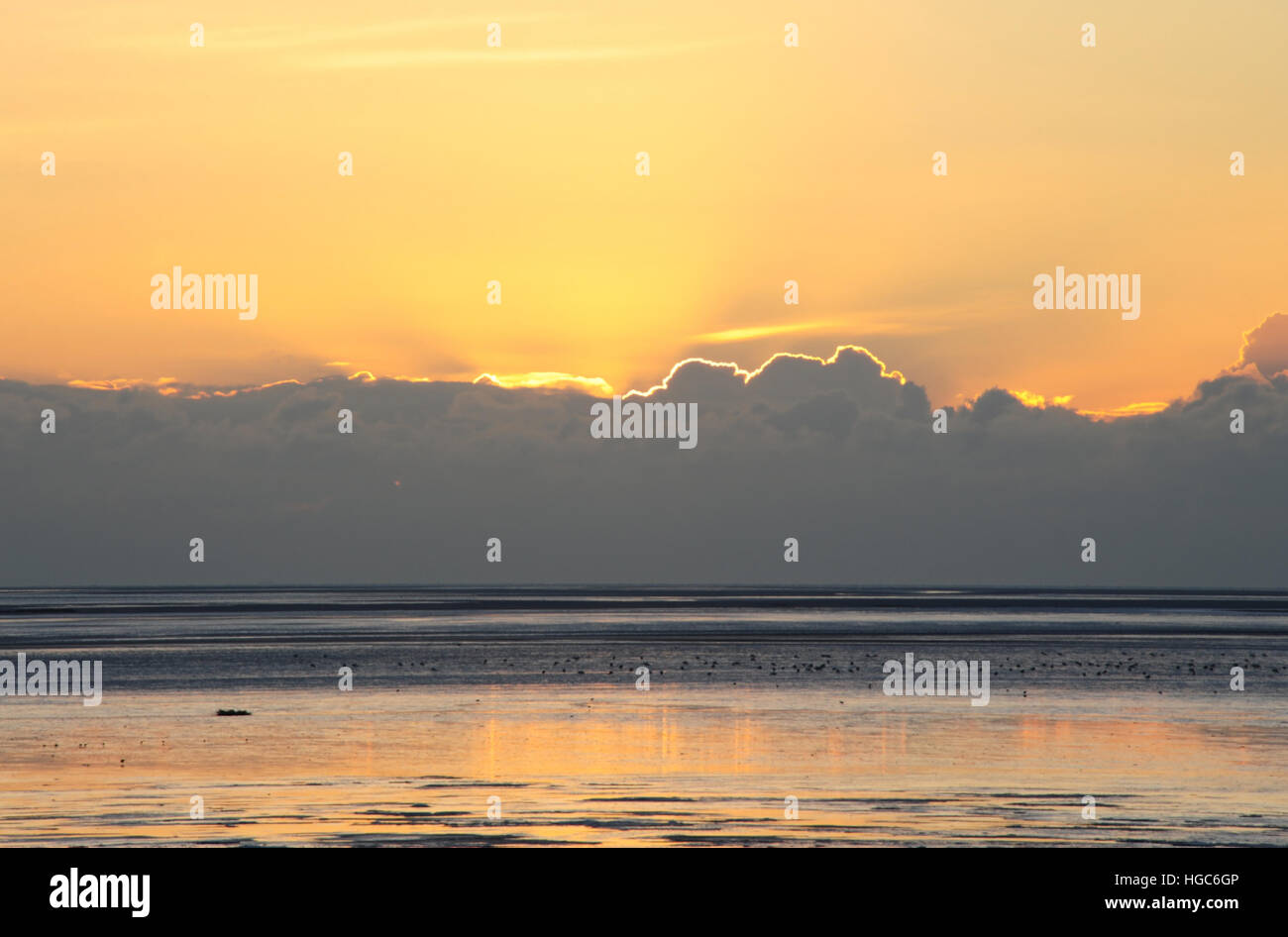 Wet sand beach view towards yellow orange sky with sunset rays rising above grey cumulonimbus clouds, St Annes, Lancashire, UK Stock Photo