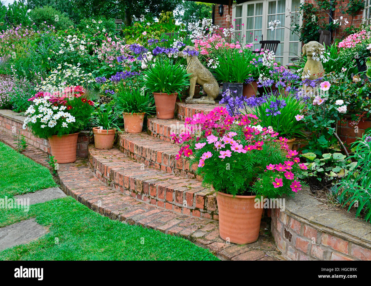 Colourful garden terrace with mixed flower beds and planted containers making a very attractice display in front of a country house Stock Photo