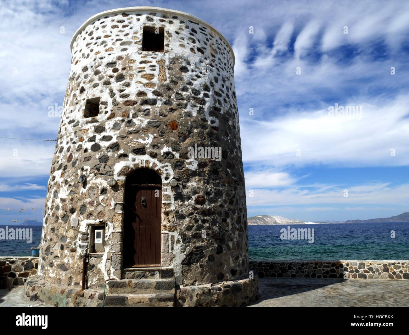 A disused Greek windmill building, with the sea and islands in the distance. Stock Photo