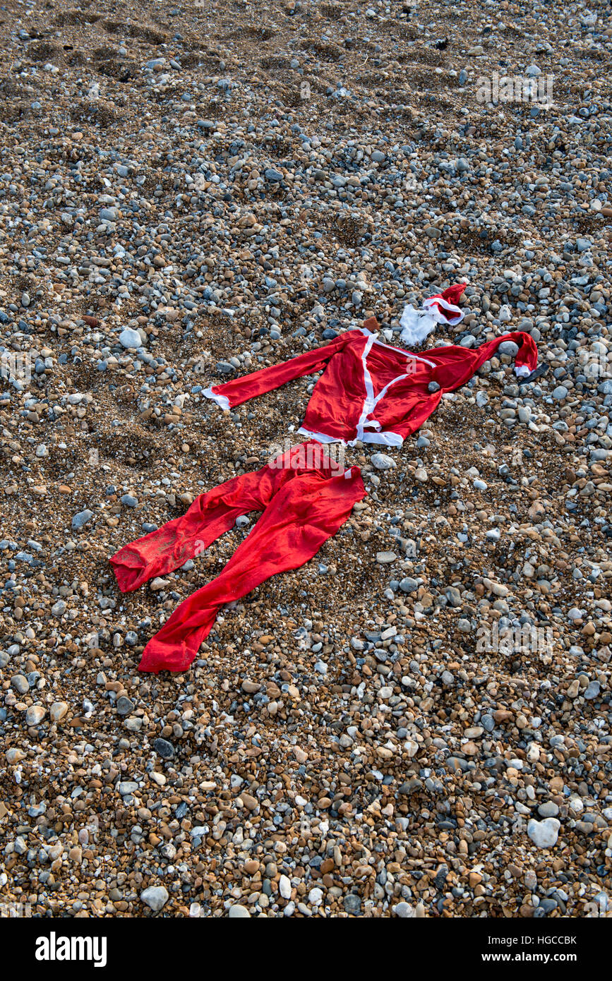 A discarded Santa suit on a pebble beach marks the end of Christmas Stock Photo