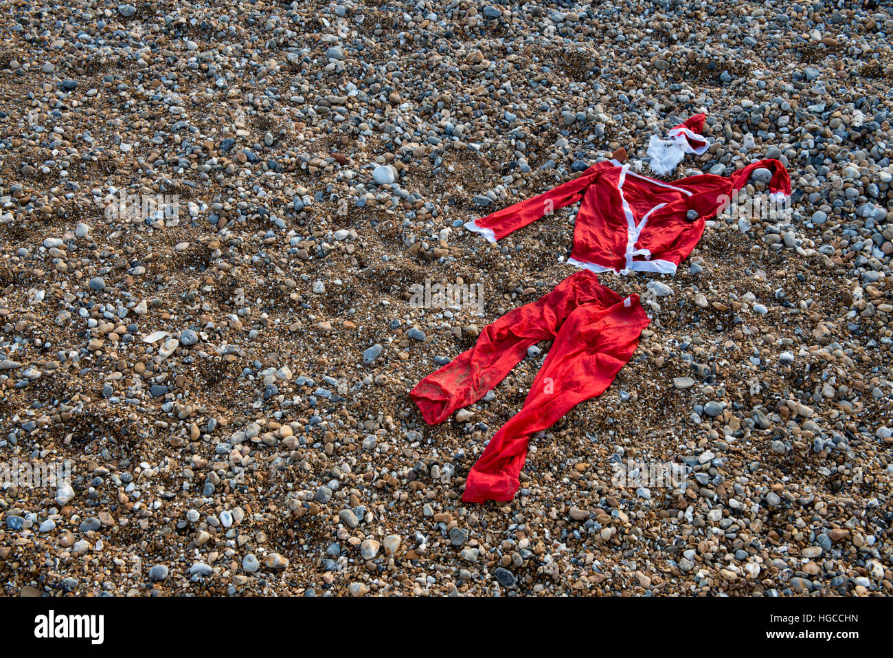 A discarded Santa suit on a pebble beach marks the end of Christmas Stock Photo