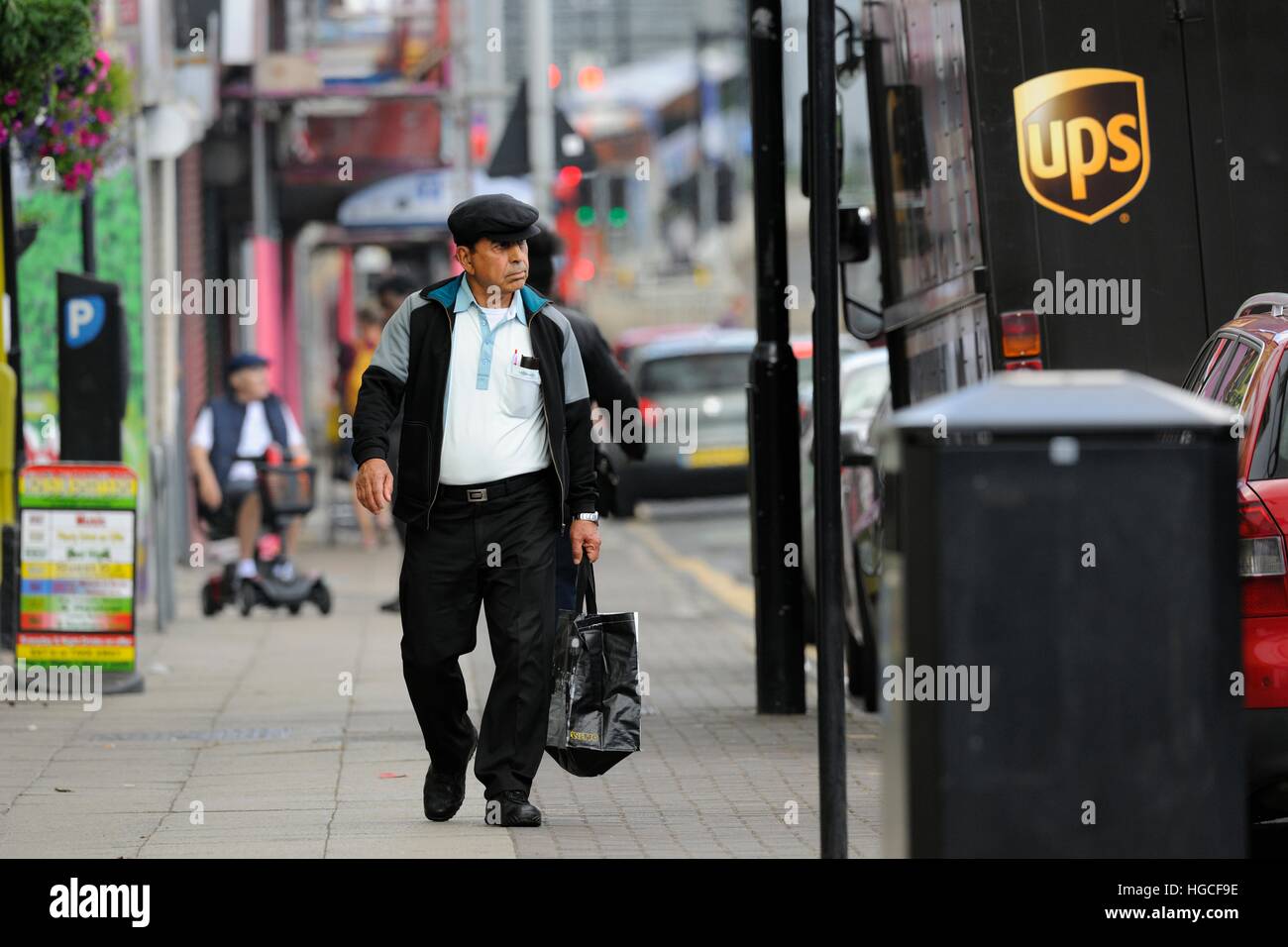 middle-aged man walking along a city street carrying a hold-all, a UPS delivery van parked on the right Stock Photo