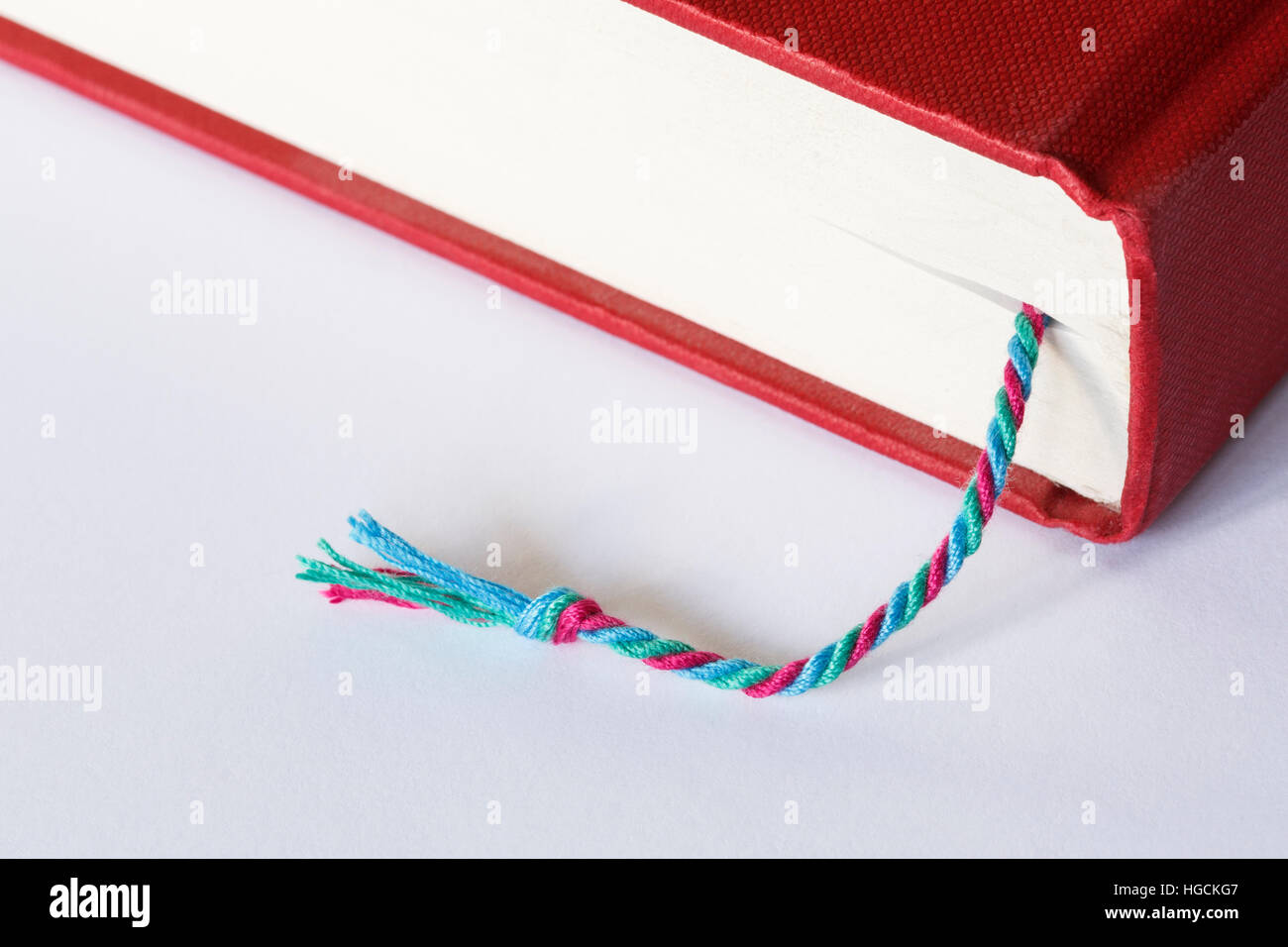 Bookmark marking a page in a closed red hardback book on a plain white table surface Stock Photo