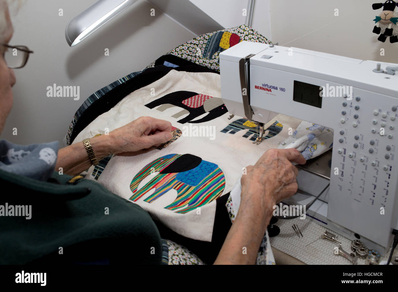 Hands of elderly woman using Bernina sewing machine for quilting bedspread with colour elephant motifs iUK Stock Photo