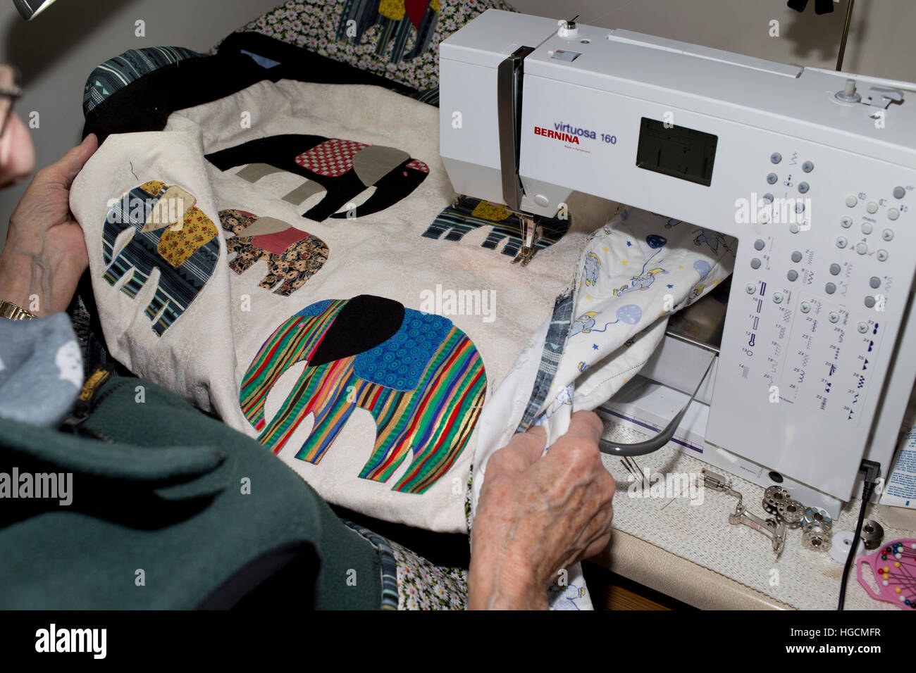 Hands of elderly woman using Bernina sewing machine for quilting bedspread with colour elephant motifs UK Stock Photo