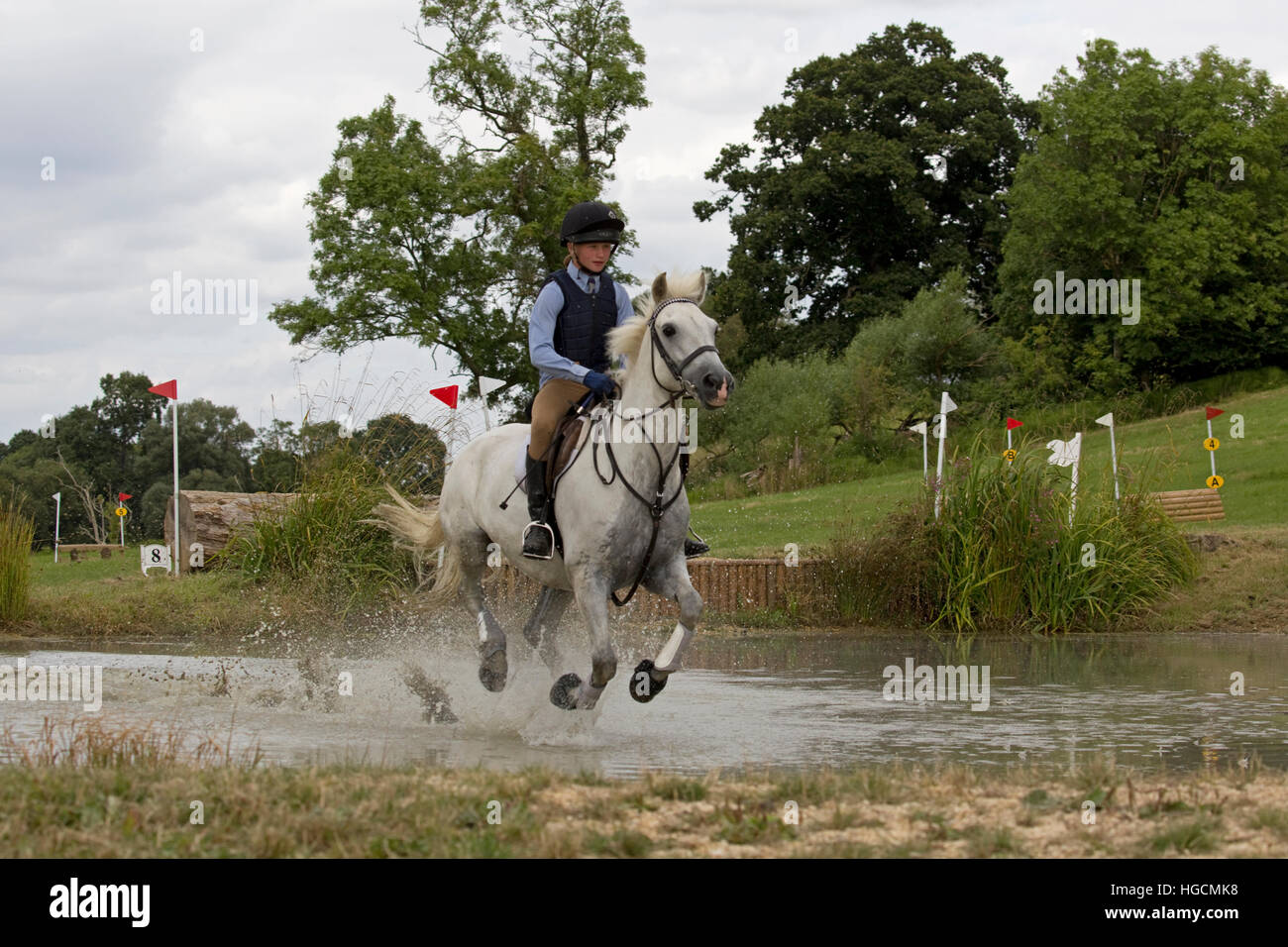Young pony club rider on white horse galloping through water jump Cotswold Pony Club camp