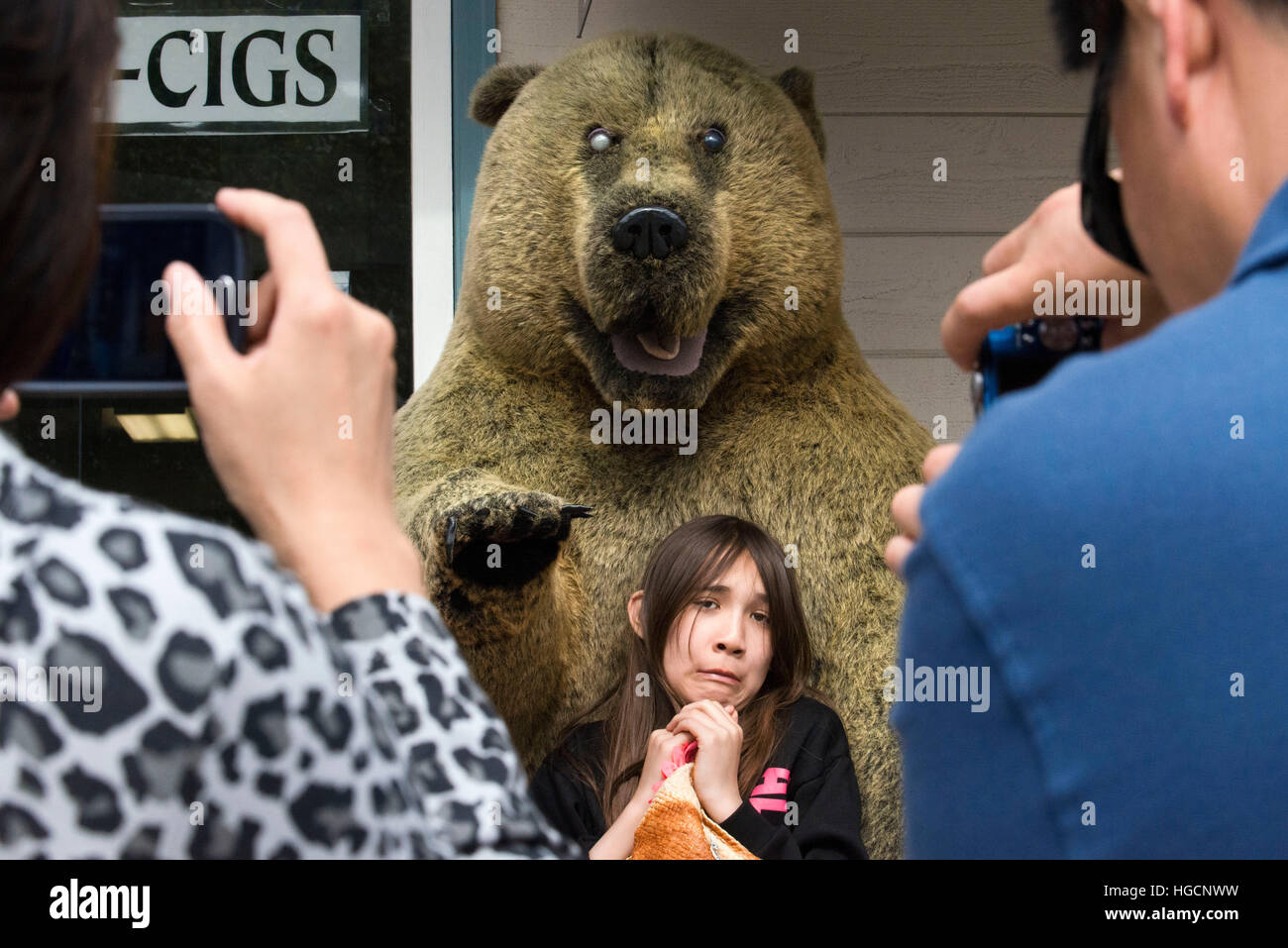 Shops in Downtown. Fear. Asian tourists photographing her daughter next to a stuffed bear. S Franklin street. Alaska Shirt Company. Alaska, USA.  The Stock Photo