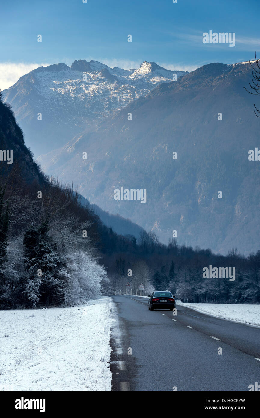 Road running through snowy landscape towards mountains with car Stock Photo