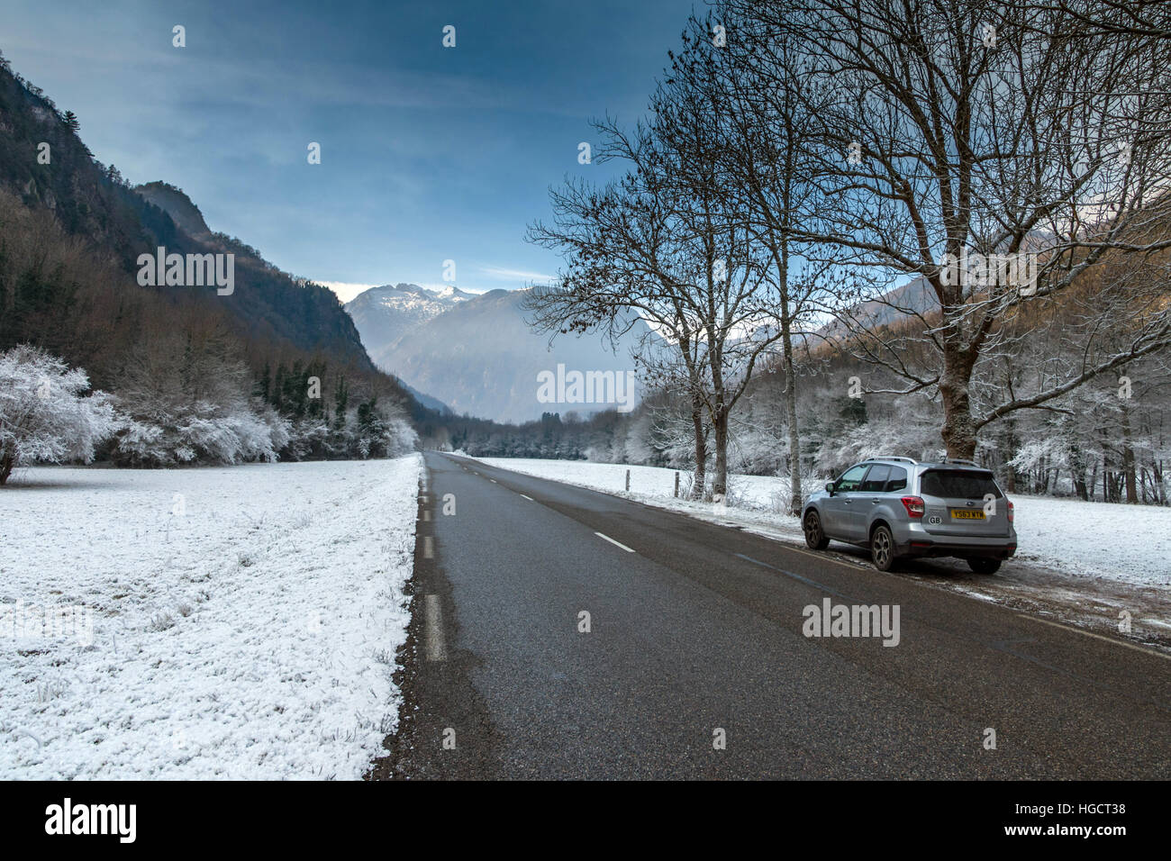Road running through snowy landscape towards mountains with parked 4x4 car, Stock Photo