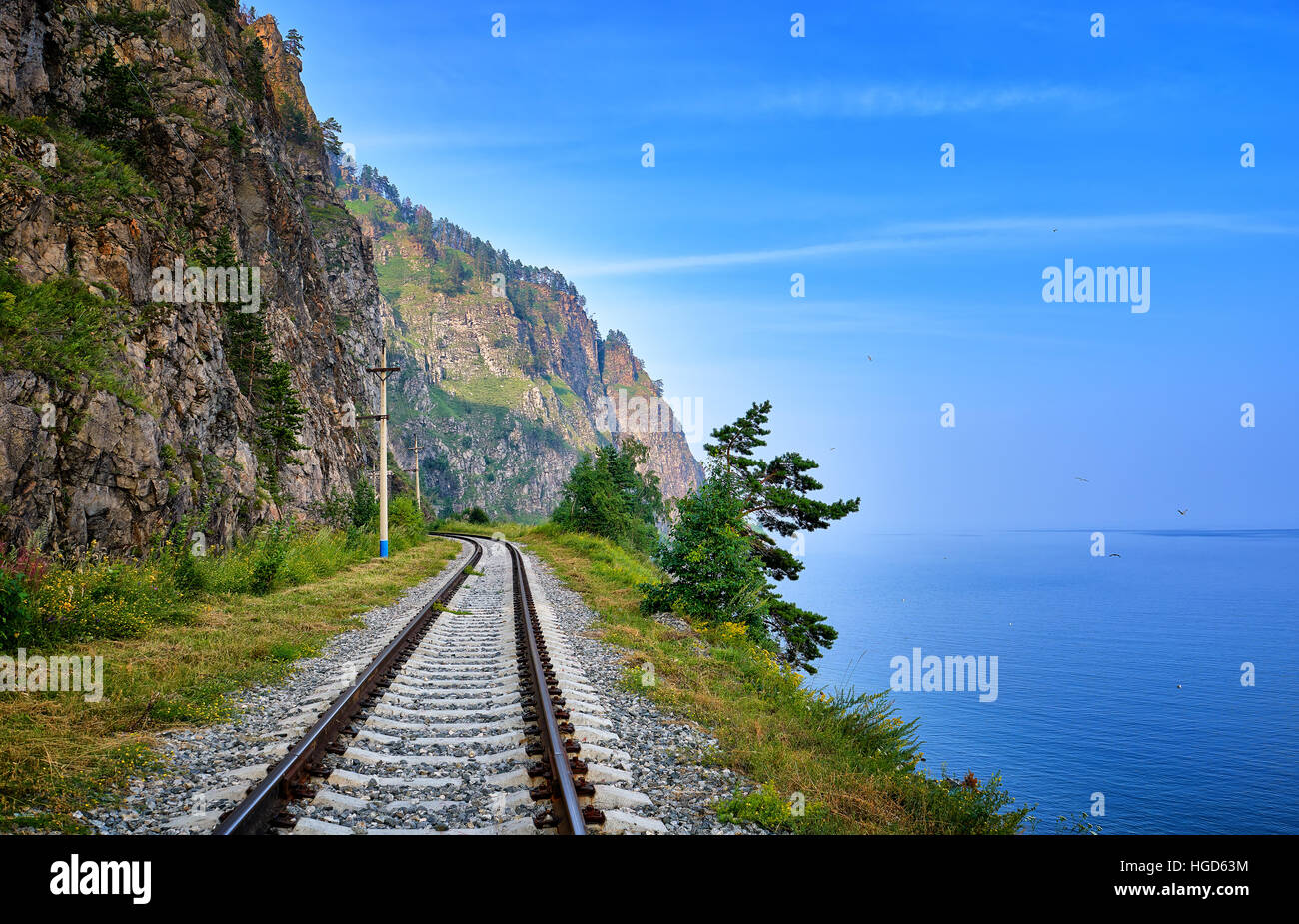 Single track railway line on edge of land between steep rock and Lake Baikal. Irkutsk region. Russia Stock Photo