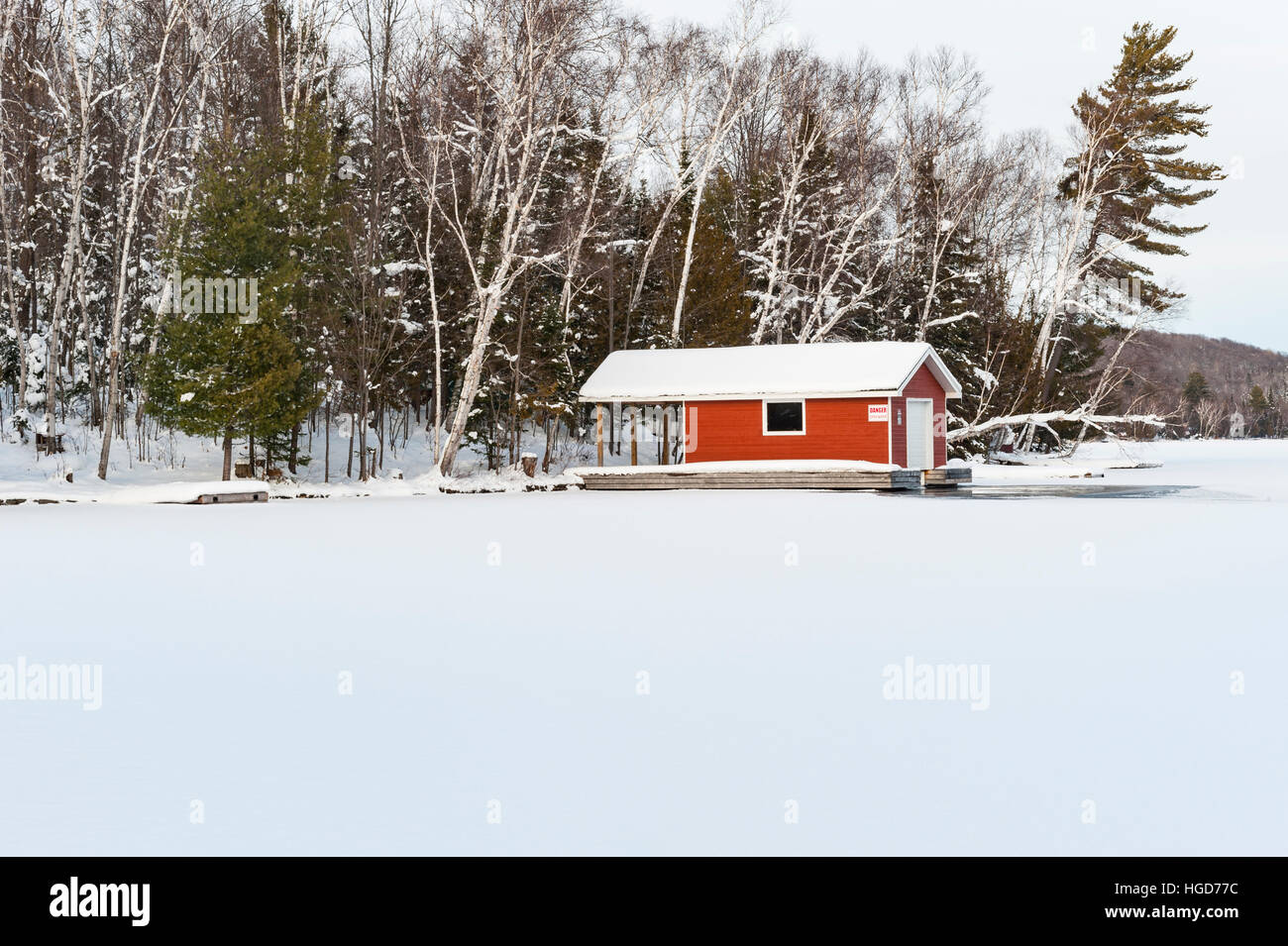 Red boathouse in a frozen lake in the Winter close to Huntsville, Ontario, ON, Canada. Stock Photo