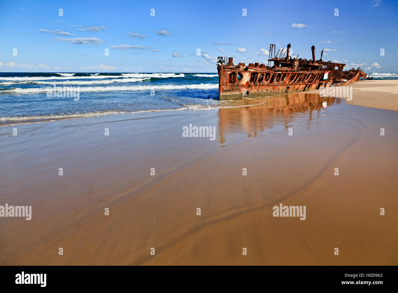 Maheno SS shipwreck on sandy beach of Fraser island against open pacific ocean horizon. Empty beach soaks smooth shallow waves reflecting rusty Stock Photo