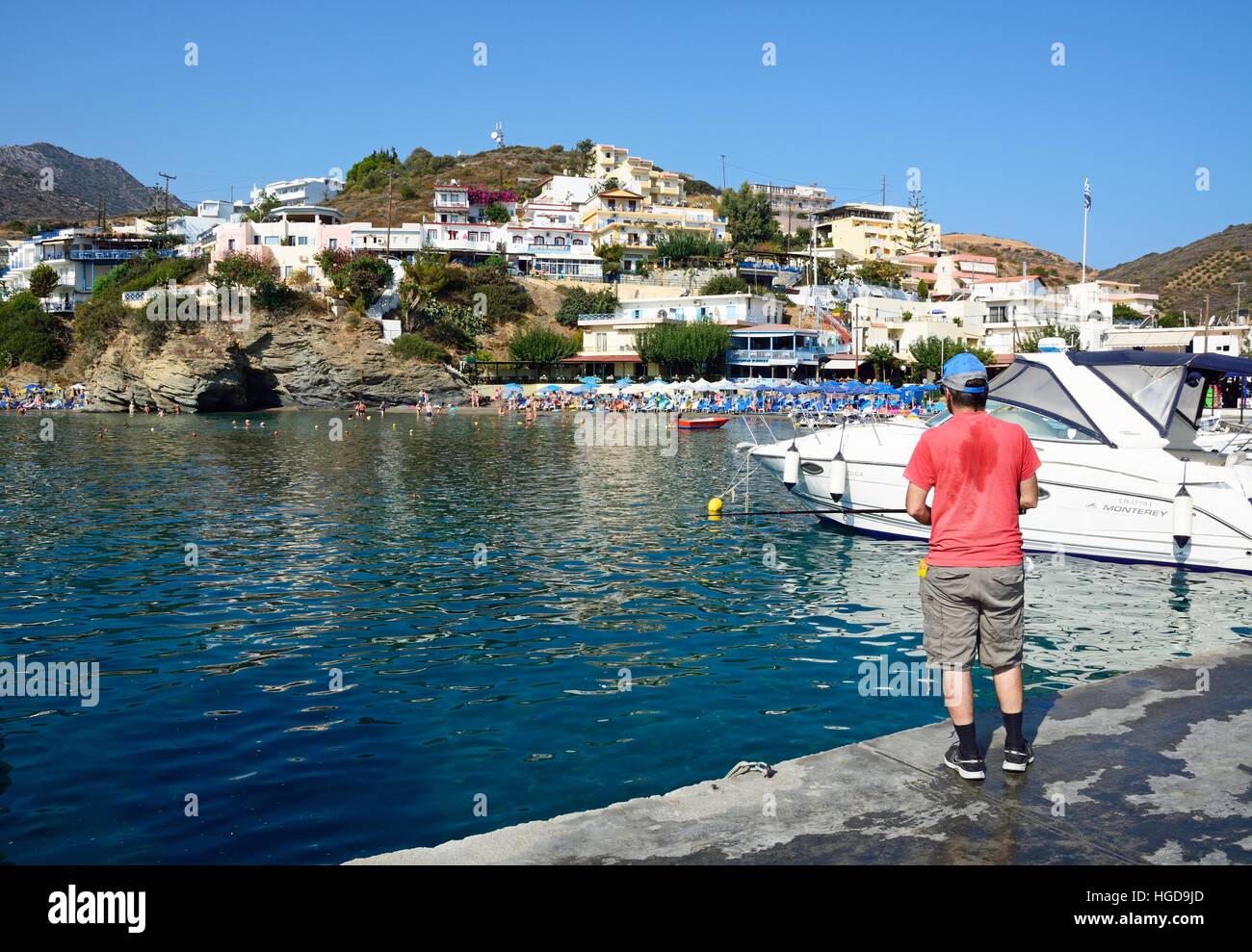 Man wishing from the harbour wall with tourists relaxing on the beach to the rear, Bali, Crete, Greece, Europe. Stock Photo