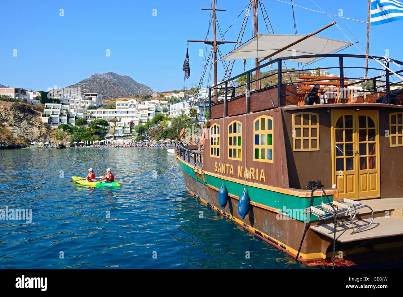 Santa Maria Galleon ship in the harbour with a couple canoeing and tourists relaxing on the beach to the rear, Bali, Crete, Greece, Europe. Stock Photo