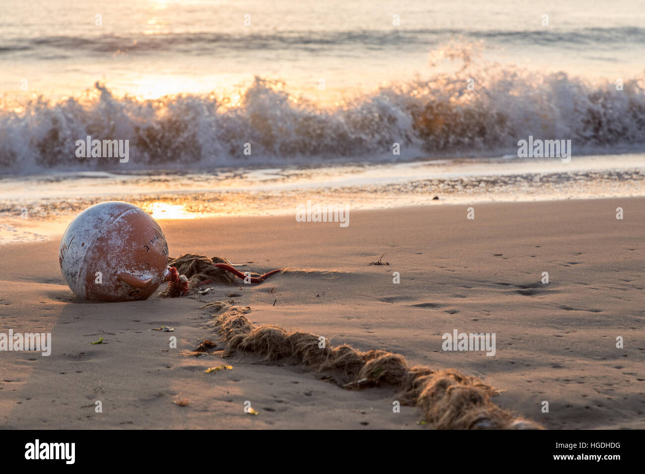 buoy and old worn rope beached on sand in bay at sunrise Stock Photo