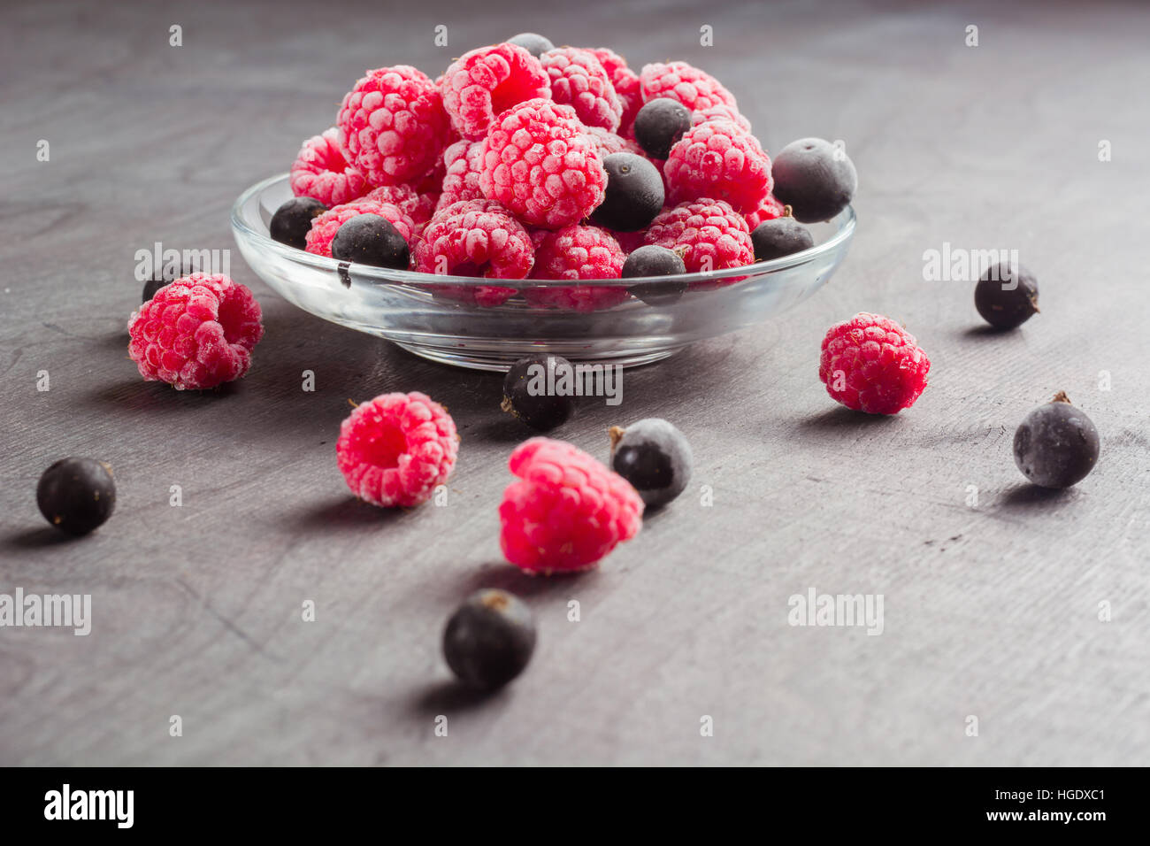 Frozen raspberries in a glass saucer. Frost on the berries. Dark ...