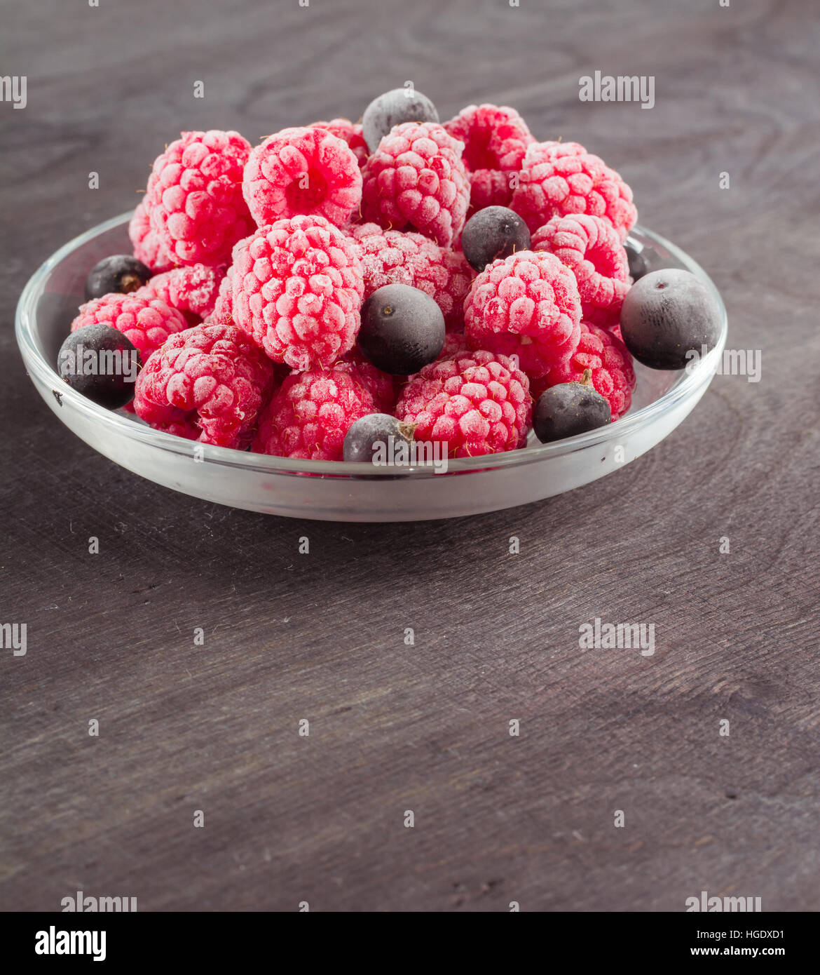 Frozen raspberries in a glass saucer. Frost on the berries. Dark ...