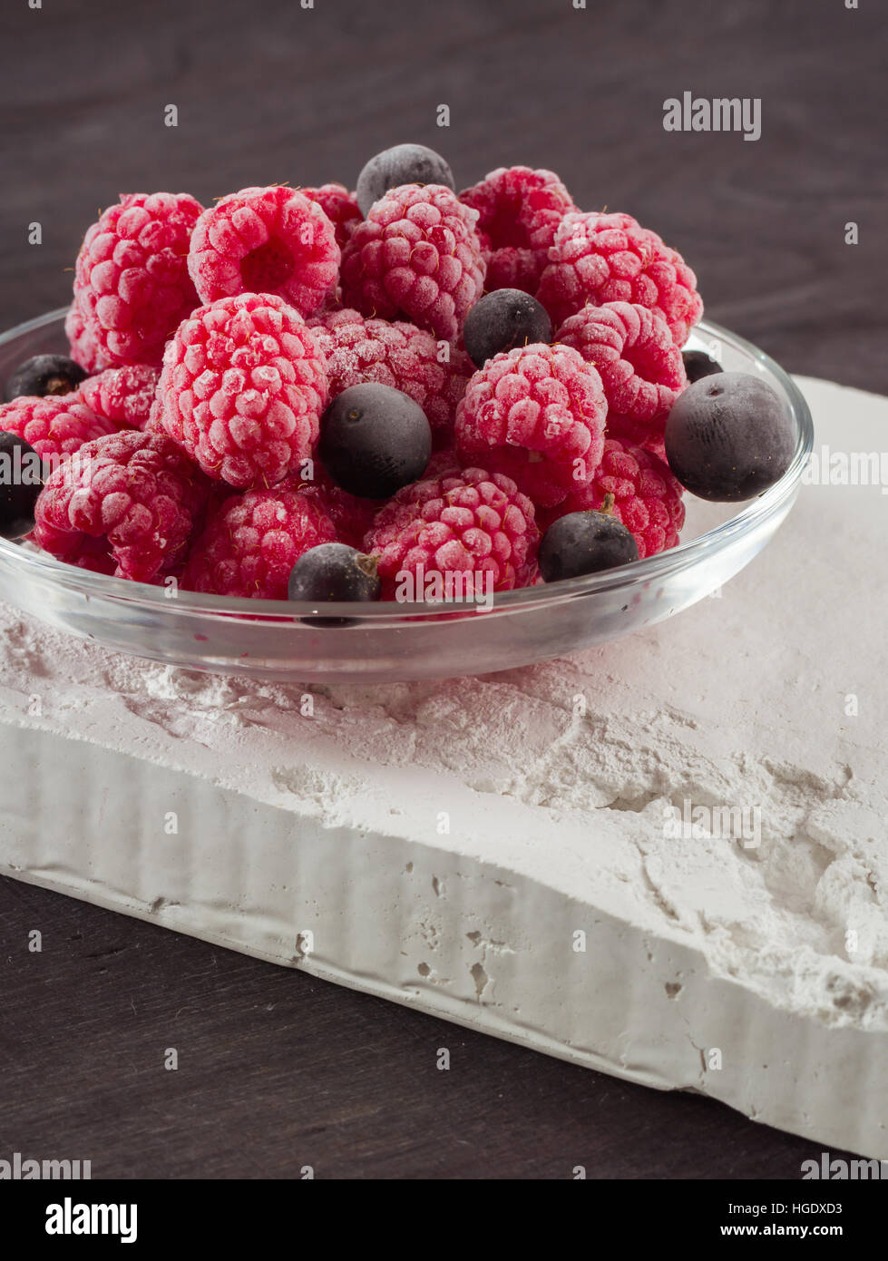 Frozen raspberries in a glass saucer. Frost on the berries. Dark ...