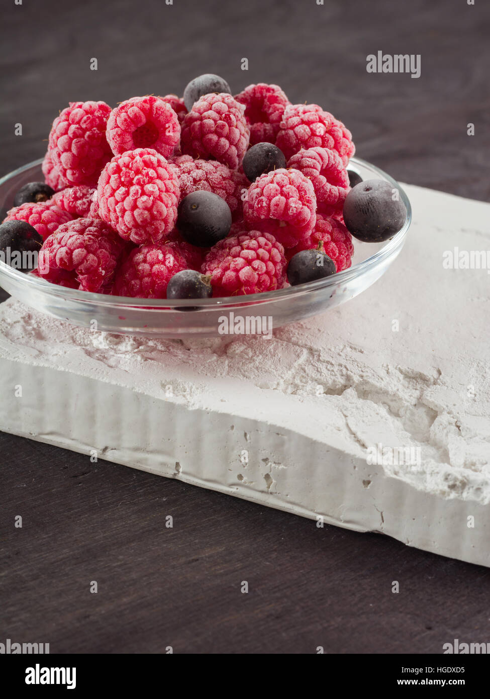 Frozen raspberries in a glass saucer. Frost on the berries. Dark ...