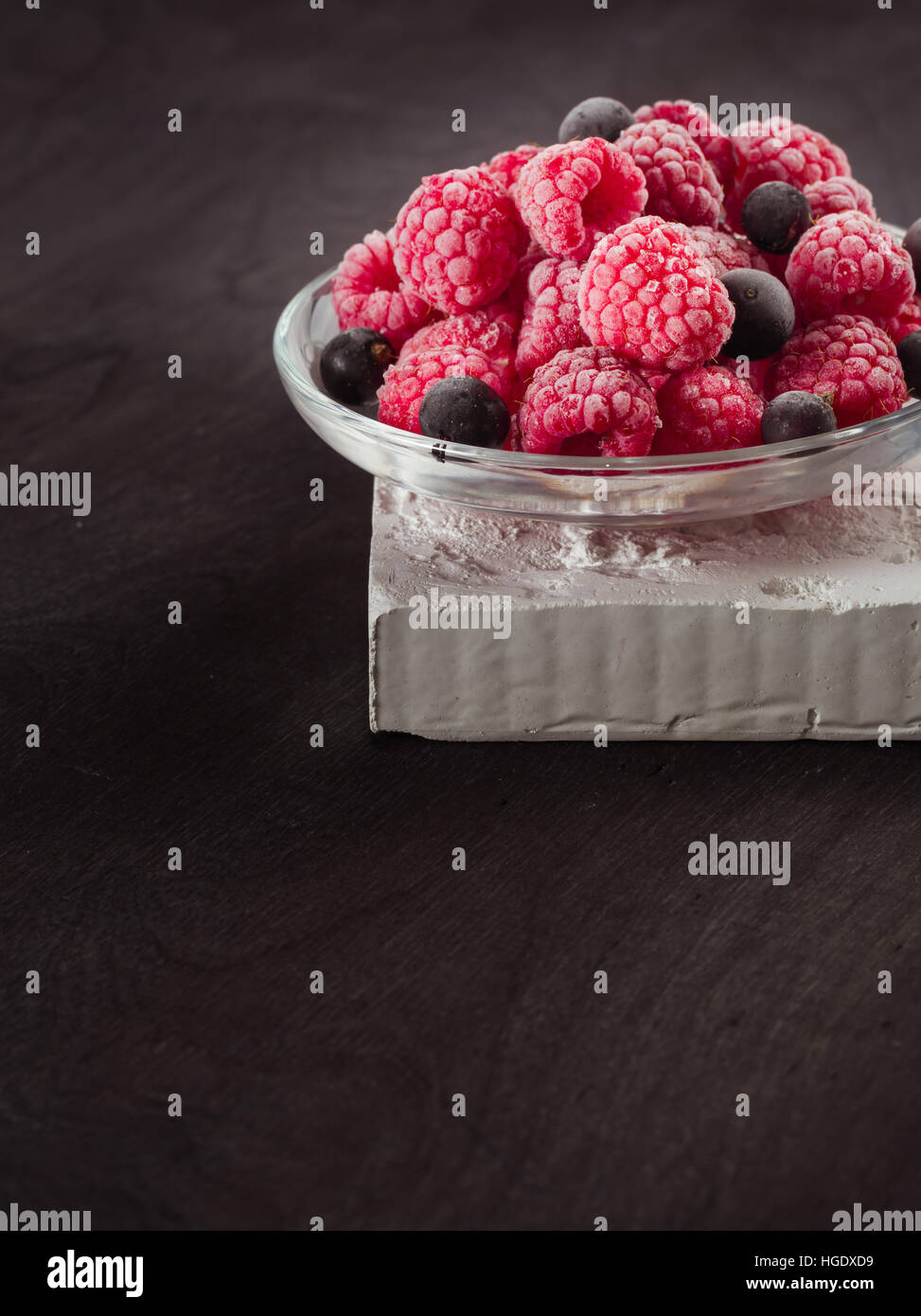 Frozen raspberries in a glass saucer. Frost on the berries. Dark ...