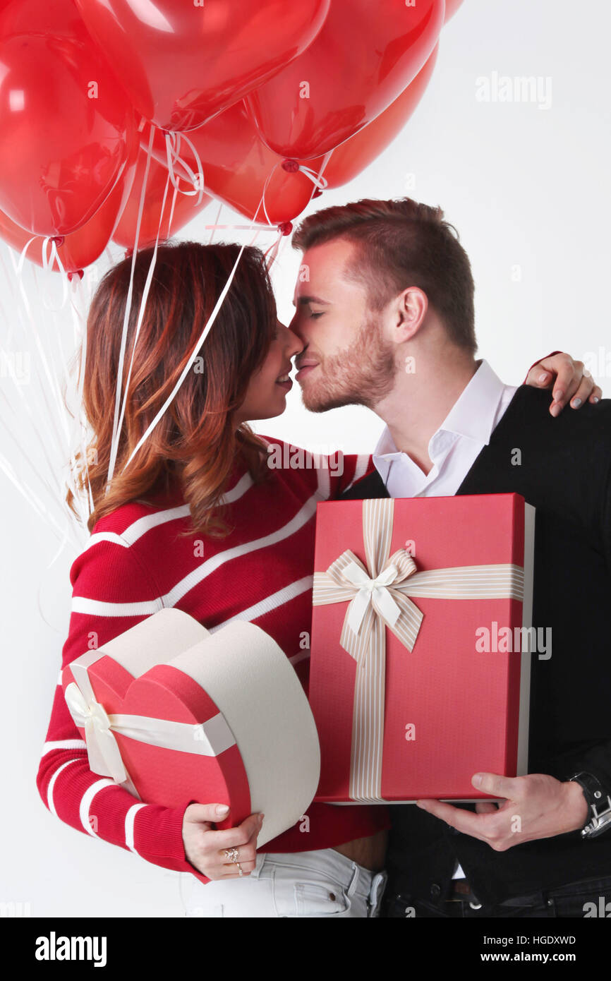 Happy kissing couple in love holding Valentines day gifts and bunch of heart shaped balloons