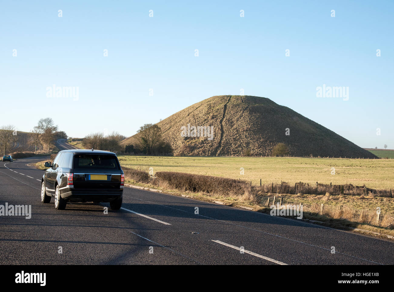 Black car on the highway passing the prehistoric Silbury Hill site near Avebury in Wiltshire England UK Stock Photo