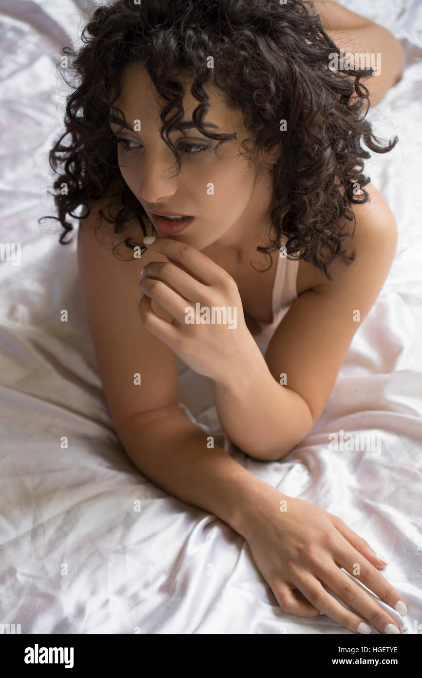 Pensive young woman laying down in bed looking away Stock Photo