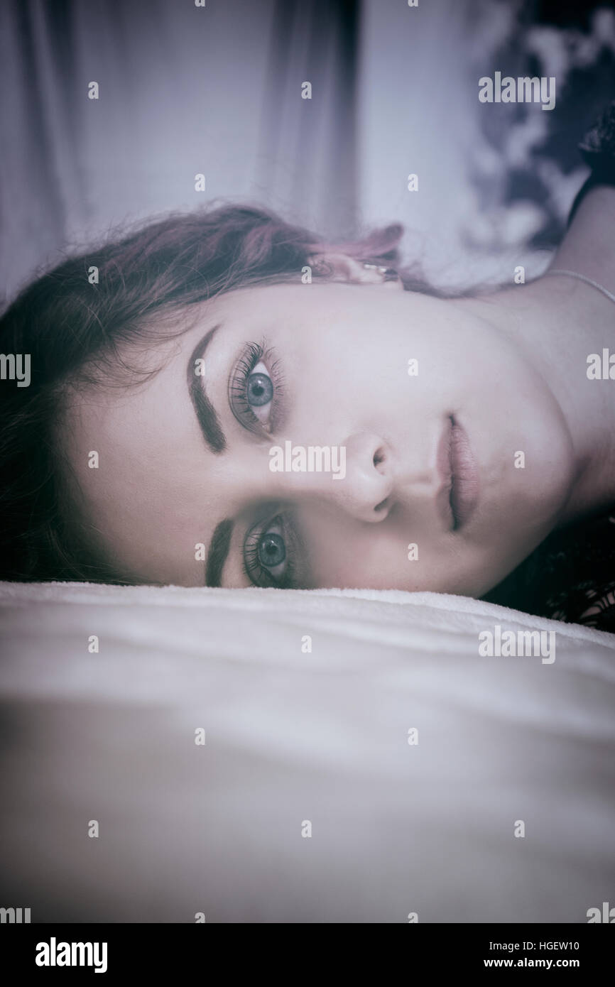 Sad woman laying down in bed staring Stock Photo