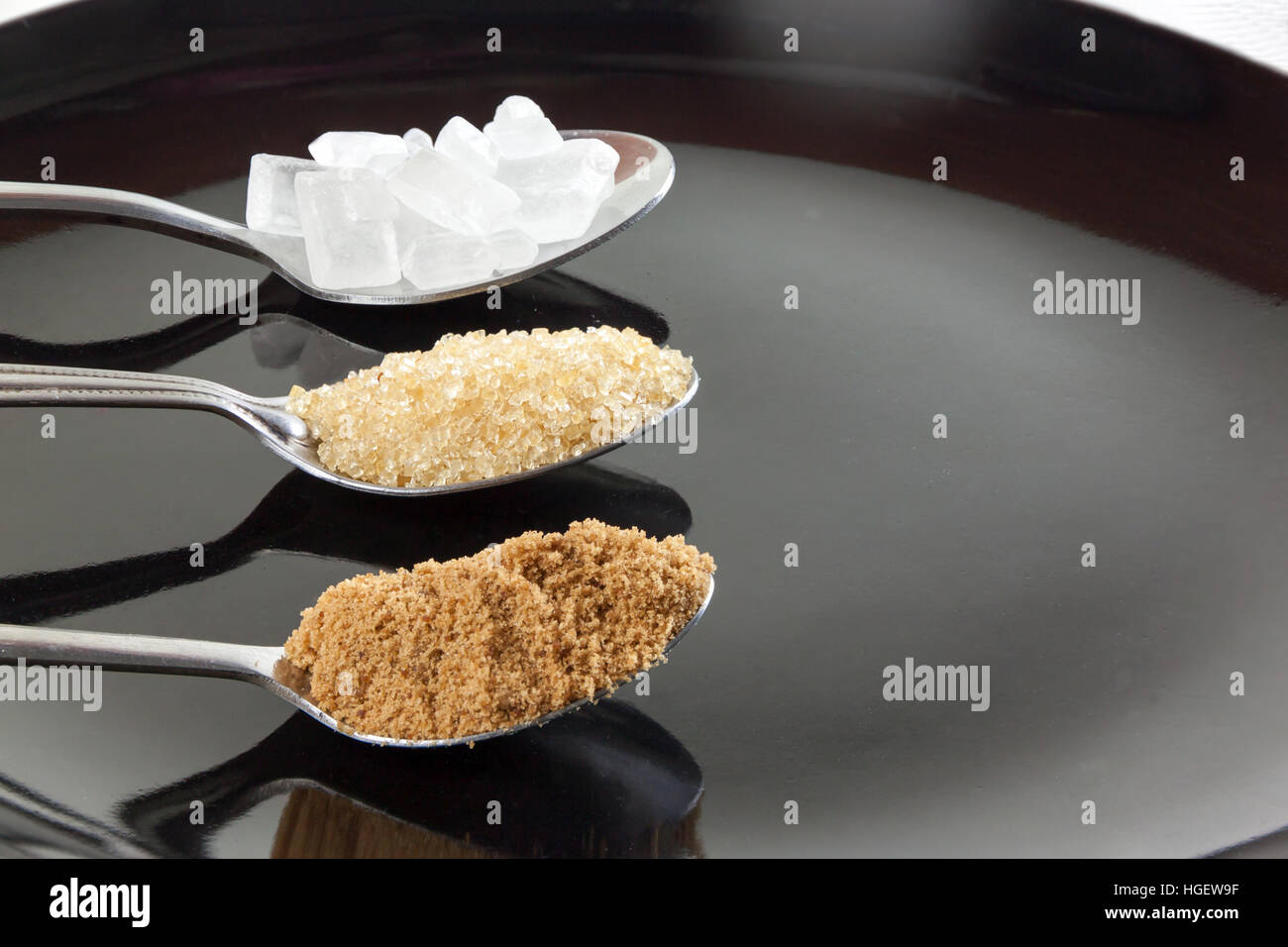 Brown cane sugar and granulated sugar and rock sugar in a metal spoon on the black background. Pure cane sugar for natural. Stock Photo