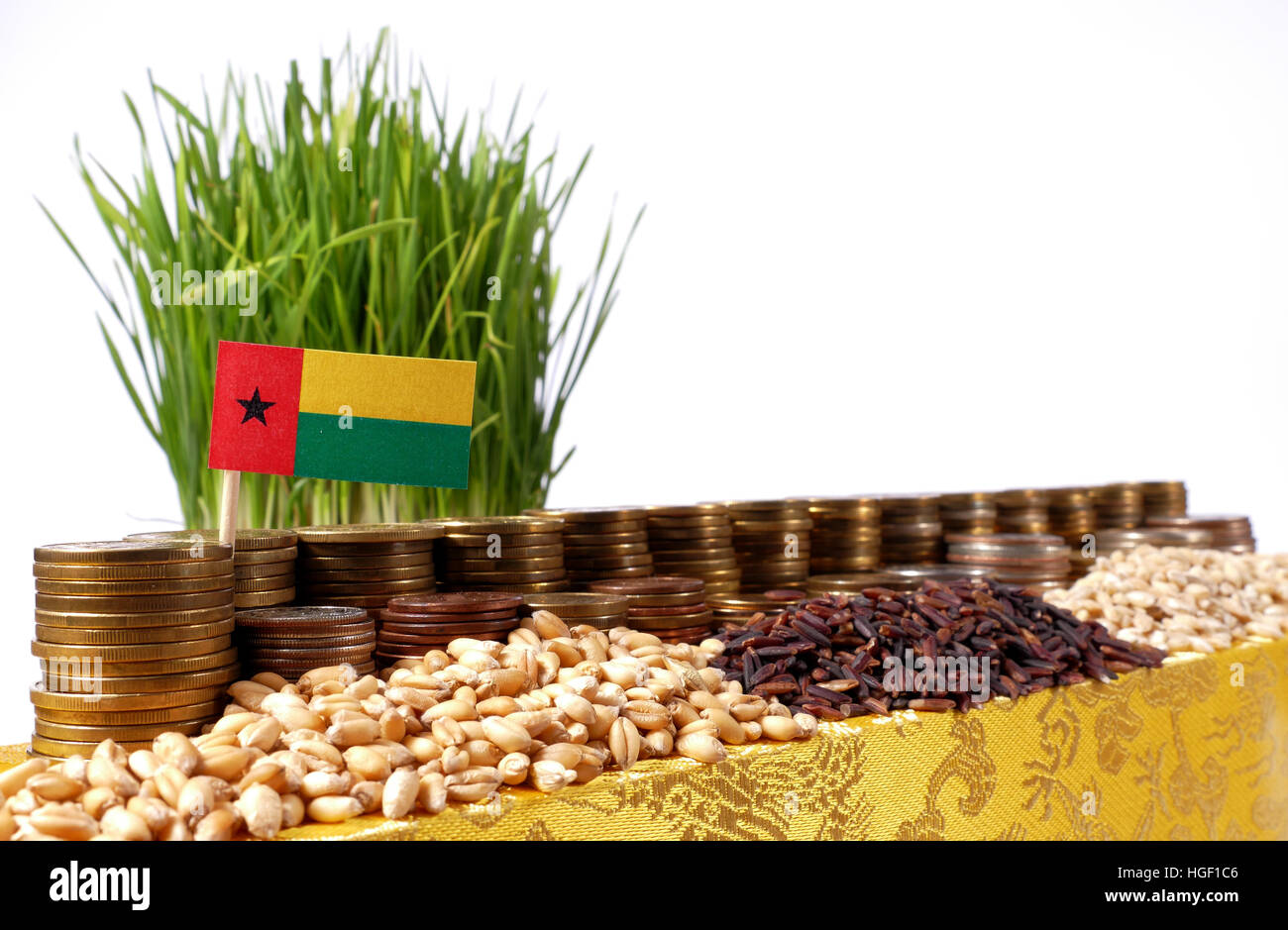 Guinea Bissau flag waving with stack of money coins and piles of wheat and rice seeds Stock Photo