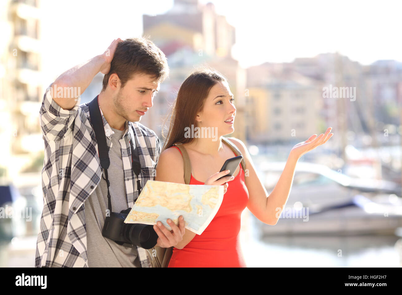 Lost couple of tourists searching location in a guide and smart phone with a port in the background Stock Photo