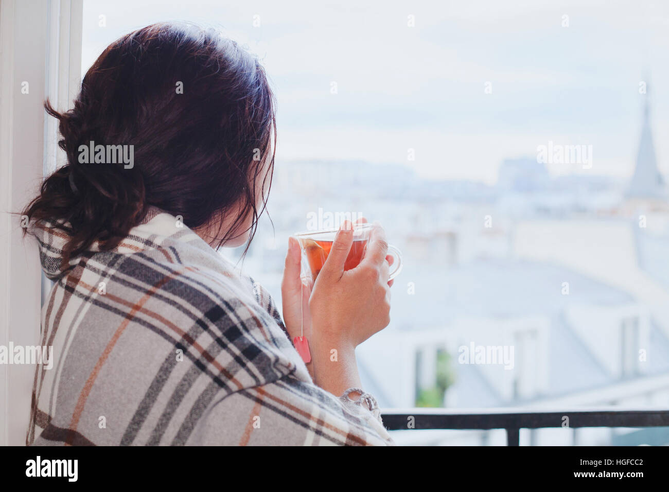 woman drinking hot tea and looking at the window, cozy winter at home, warm up, december in city, waiting Stock Photo