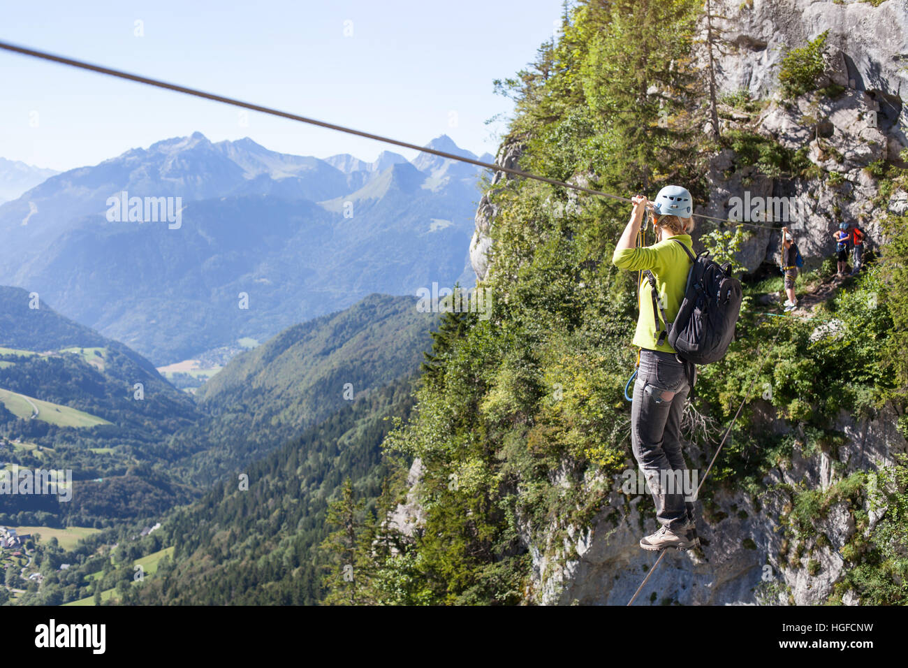 via ferrata climbing, woman in harness crossing rope bridge in the mountains, alpinism or extreme sport Stock Photo