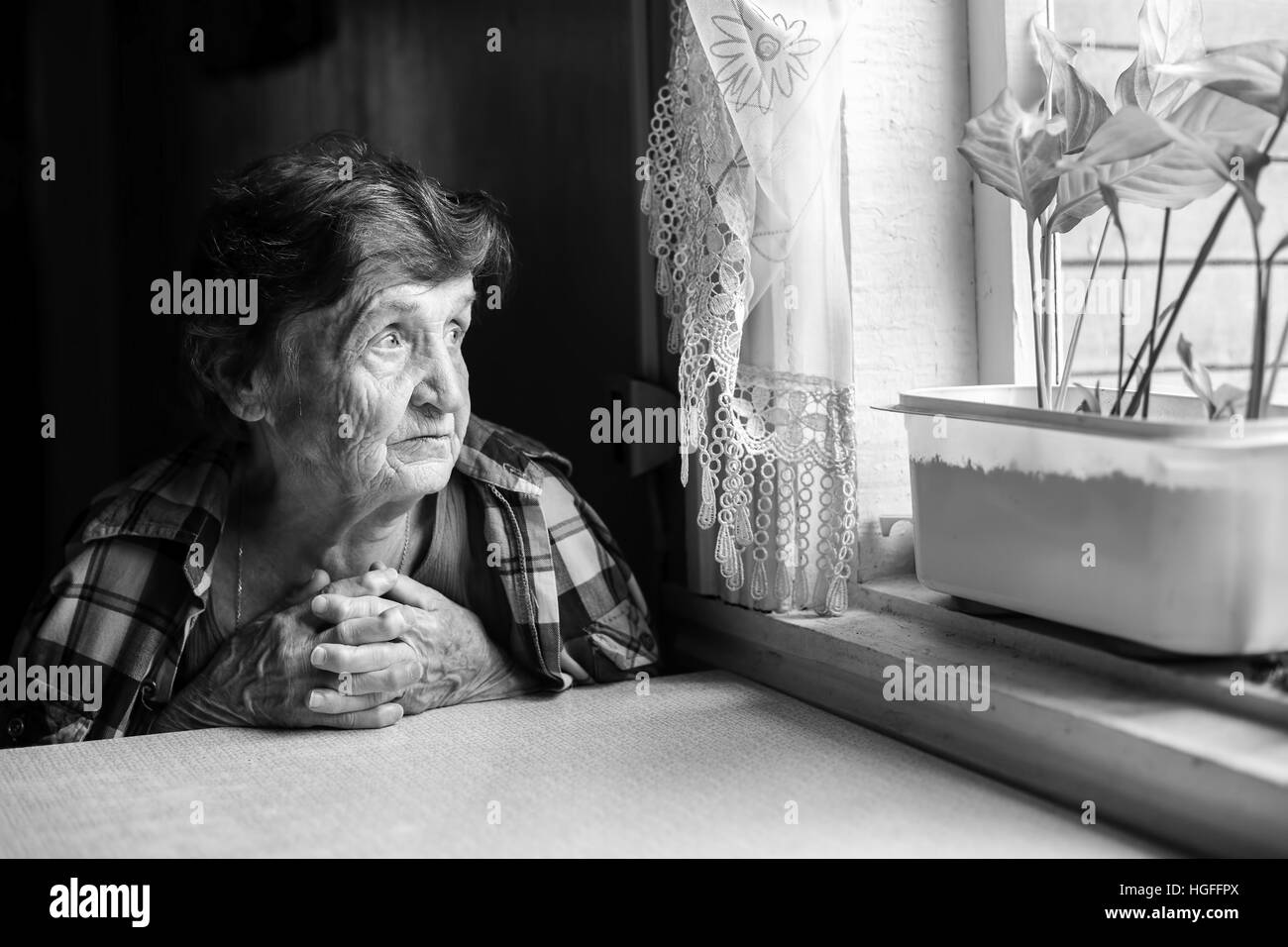 Elderly woman looks wistfully out the window. Black-and-white photo. Stock Photo