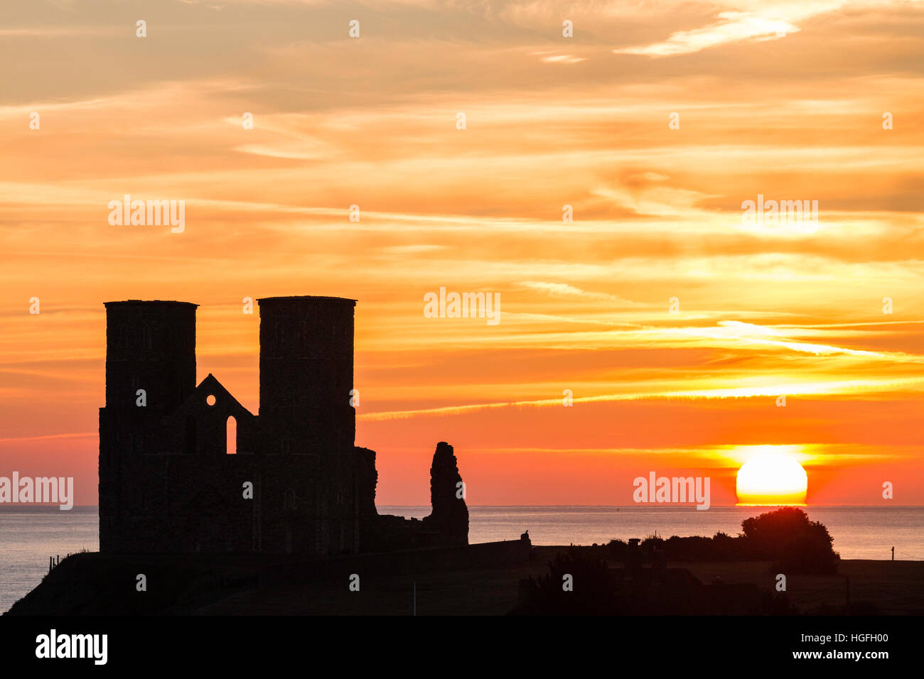 England, Reculver. Sunrise  and orange sky over the sea with silhouetted landmark twin towers of 12th century Angelo-Saxon church. Stock Photo