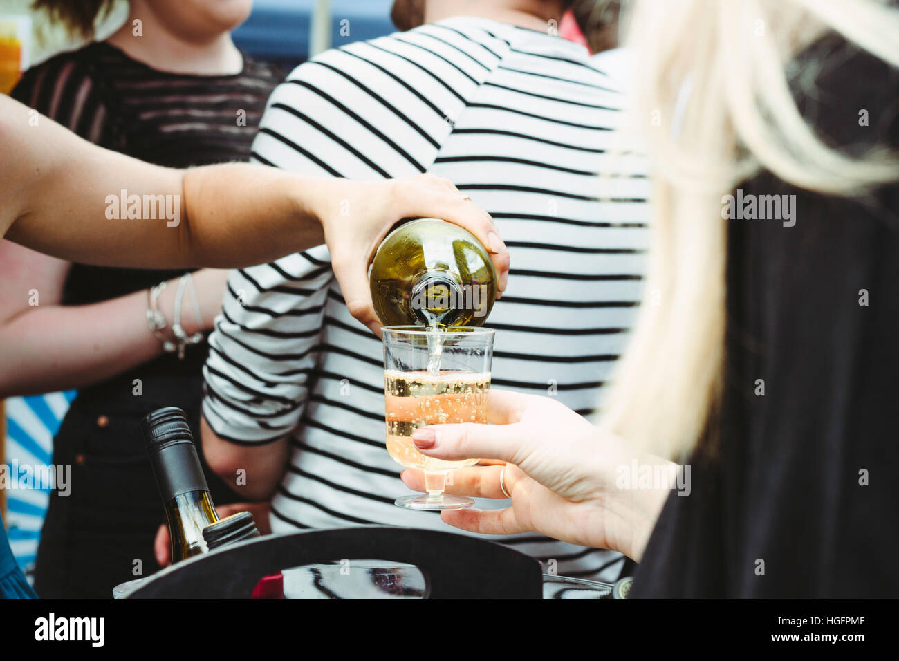 A close up of a hand pouring white wine to an unrecognisable woman in an outdoor event Stock Photo