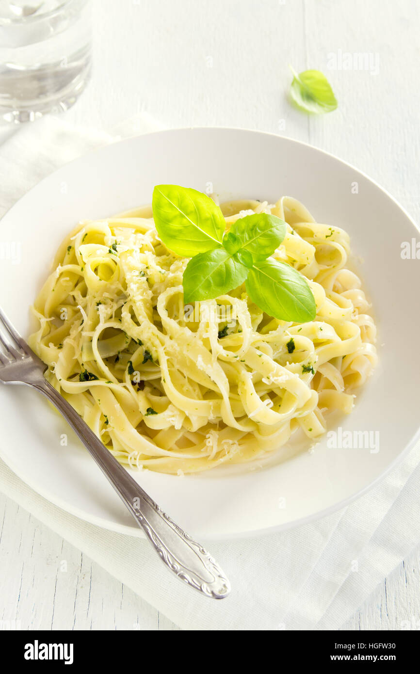 Tagliatelle pasta with pesto sauce, cheese and basil leaves on white