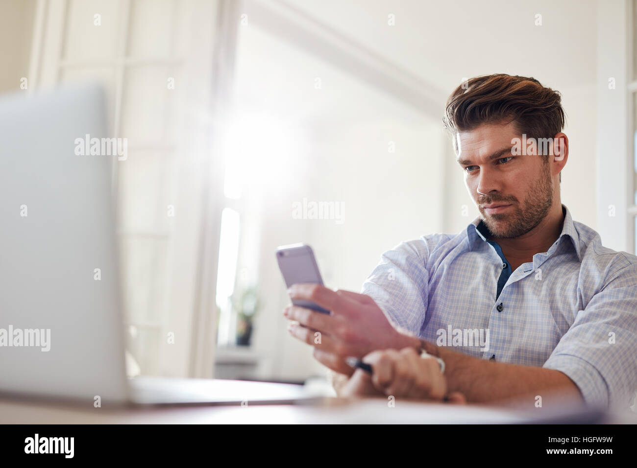 Shot of relaxed young man sitting at desk using mobile phone. Handsome caucasian man reading text message on his smart phone. Stock Photo