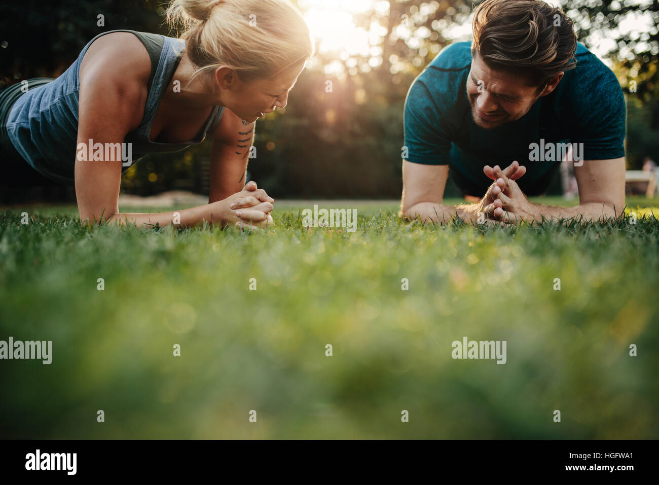 Healthy young couple exercising at park and smiling. Fit young man and woman doing core training outdoors in morning. Stock Photo