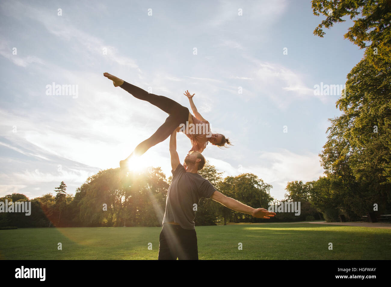 Shot of young couple doing acroyoga. Young man lifting and balancing woman on his hand at the park. Stock Photo