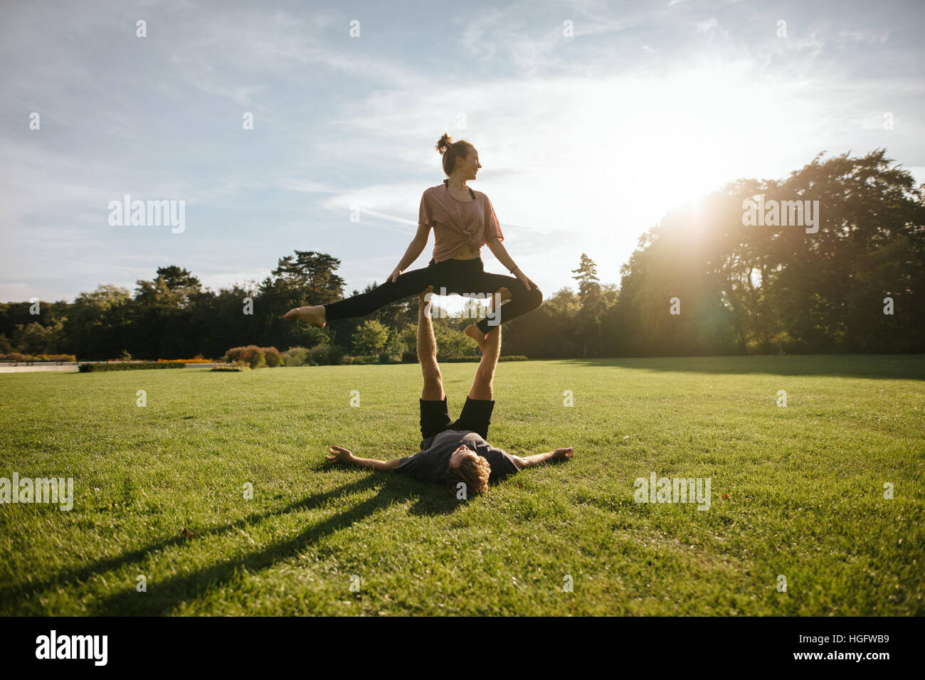 Fit young couple doing acroyoga on grass. Man and woman in park practising pair yoga poses in sunny morning. Stock Photo