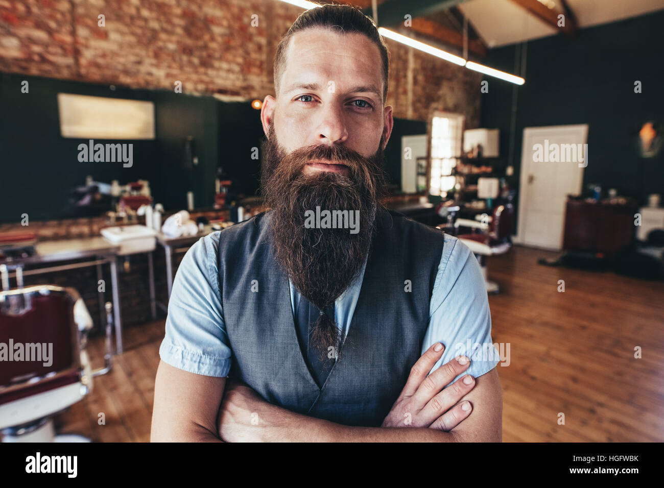 Young barber at his barbershop. Man standing with his arms crossed and staring at camera. Stock Photo