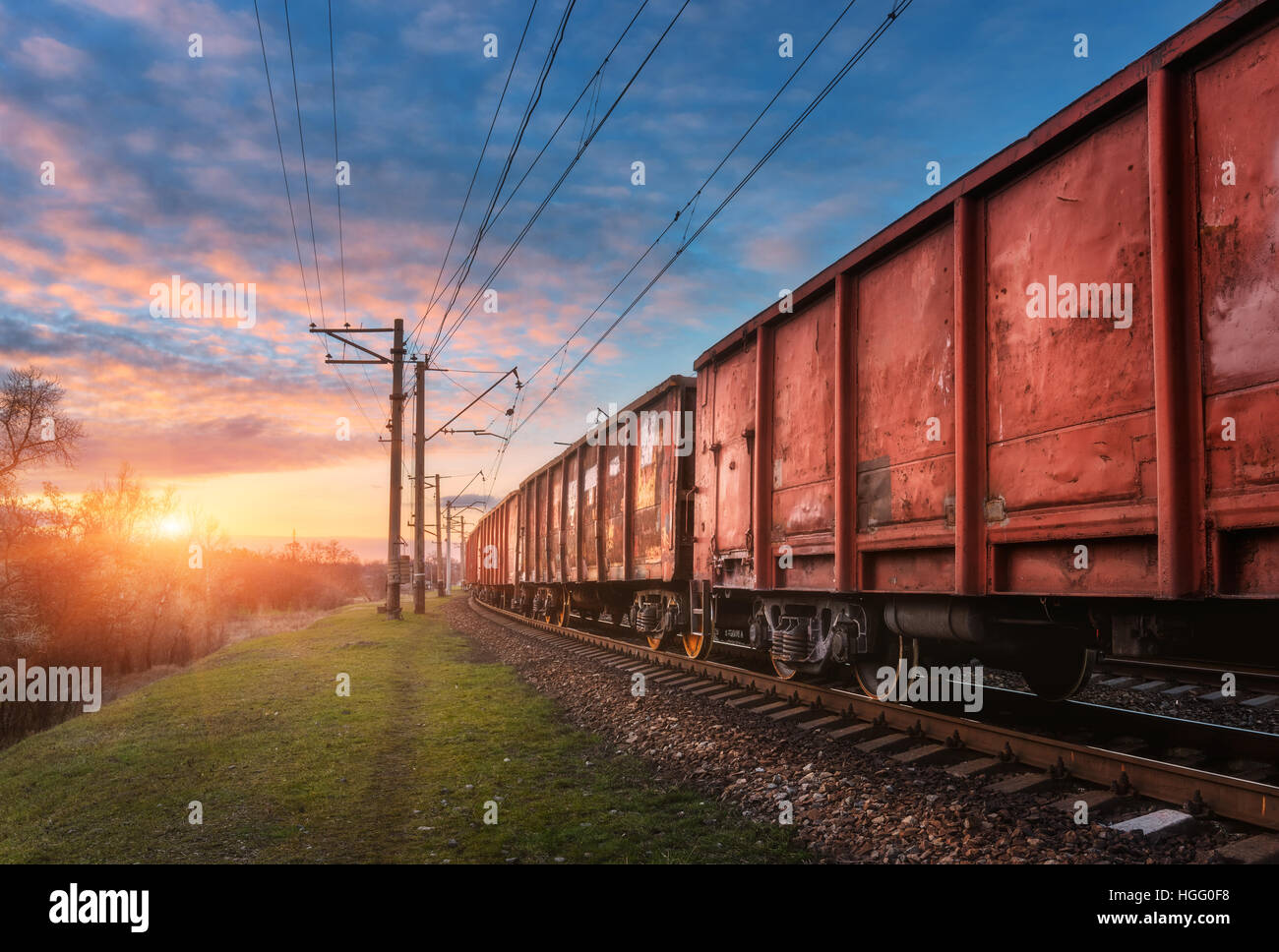 Railway station with cargo wagons and train against sunny sky with clouds in the evening. Colorful industrial landscape Stock Photo